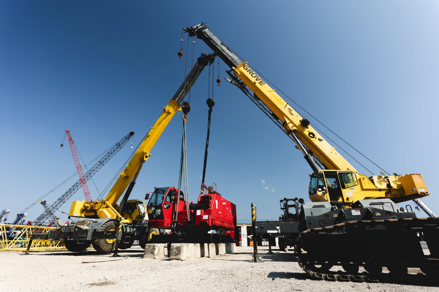 Lift cranes moving a piece of heavy equipment onto a construction site